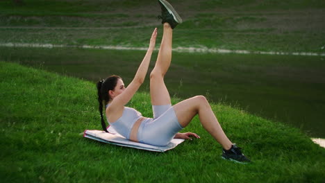 A woman does exercises for the muscles of the press lying on the grass in a Park near the lake. Work with abs muscles. Creating a beautiful body