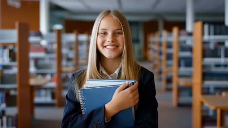 happy schoolgirl holding books in a library