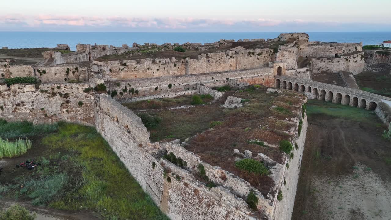 Methoni, Messenia, Peloponneso, vista aerea panoramica delle rovine del castello di Methoni, rotazione circolare a destra e indietro dopo l'ora d'oro con nuvole bianche e mare aperto all'orizzonte