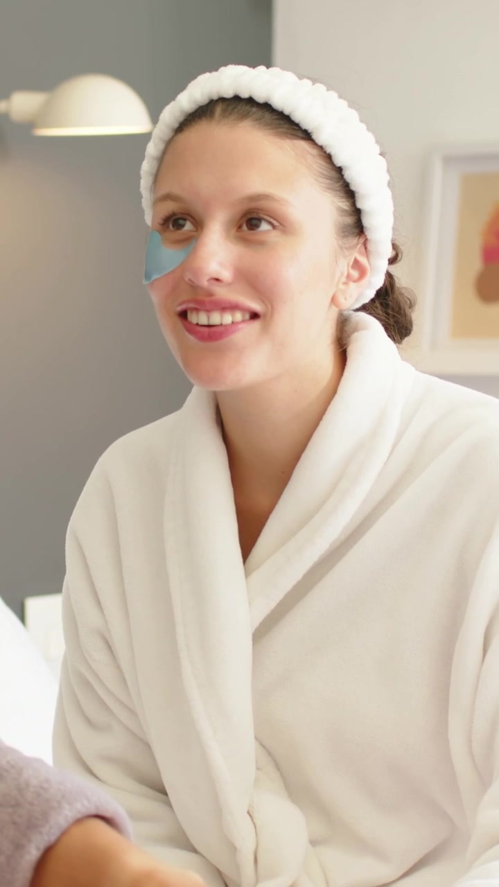 Professionista della cura della pelle preme una spugna, applicando un patch sotto gli occhi a una donna con accappatoio e fascia per capelli in una spa rilassante.