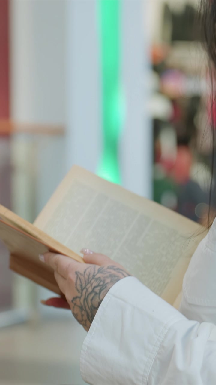 Donna con mani tatuate che tiene un vecchio libro. Rivelando parole visibili all'interno contro una luce verde soffusa. Lo sfondo presenta un'illuminazione verde sfocata e vetrine di negozi.