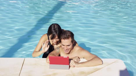 Lächelndes-Paar-Im-Schwimmbad-Verwenden-Digitales-Gerät