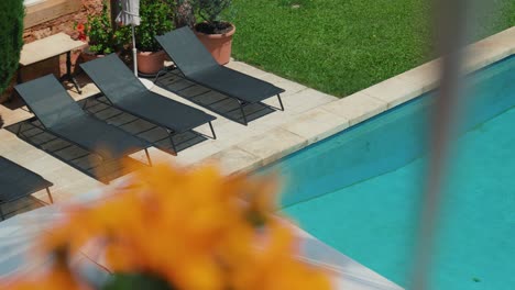 Scenic-panoramic-shot-of-sunbeds-next-to-a-clear-blue-swimming-pool-in-beautiful-castle-garden