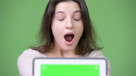 young beautiful woman showing digital tablet and looking shocked