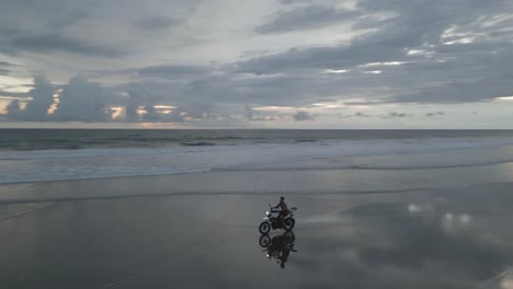 Un-Hombre-Asiático-Monta-Una-Motocicleta-En-La-Extensa-Playa-De-Bali-En-Una-Mañana-Gris