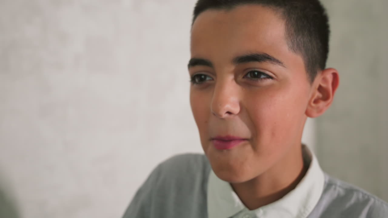 Close-up of joyful young boy making playful expression, smiling and looking excited. Casual gray shirt with white collar, background blurred, indoors, happy emotion