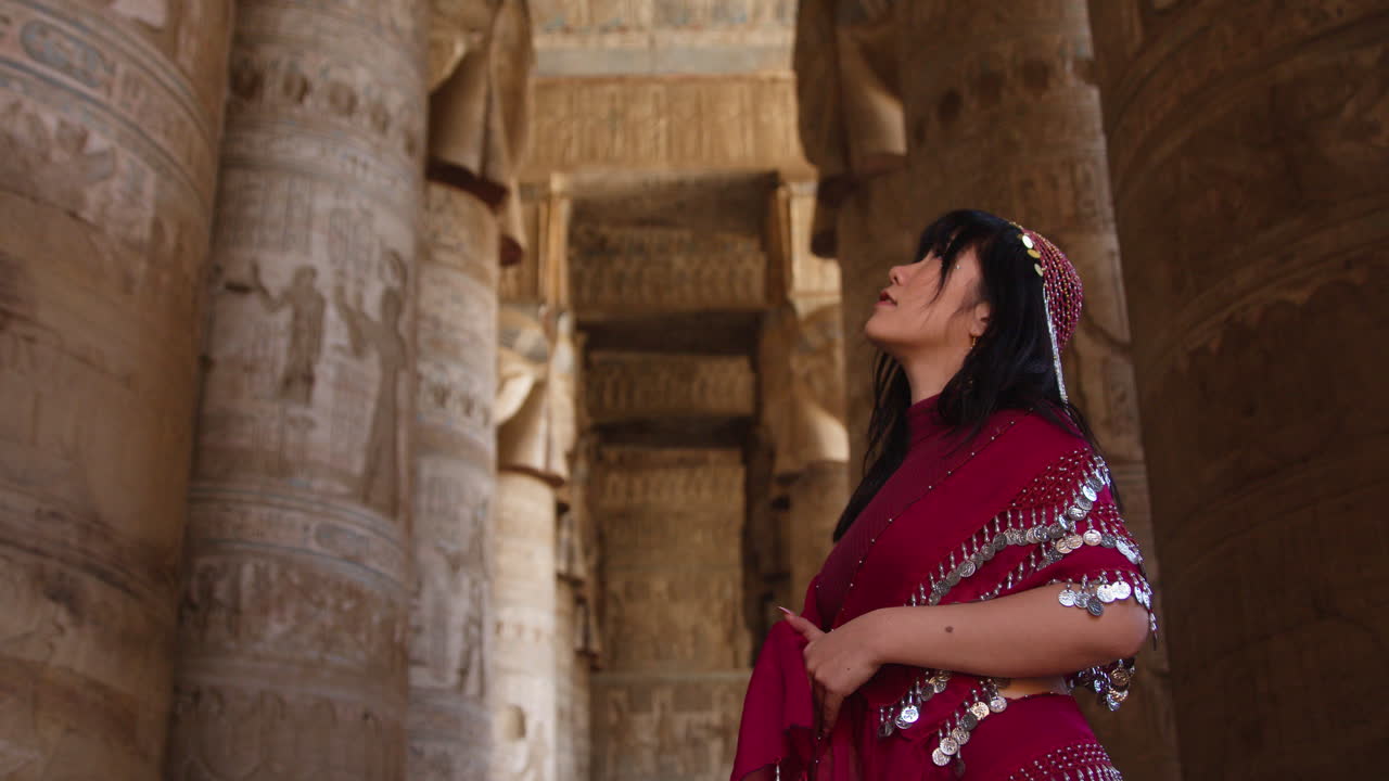 Woman in traditional outfit admires ancient columns at Dendera Temple in Egypt