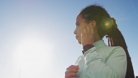 african american woman in sportswear wearing earphones on a sunny day