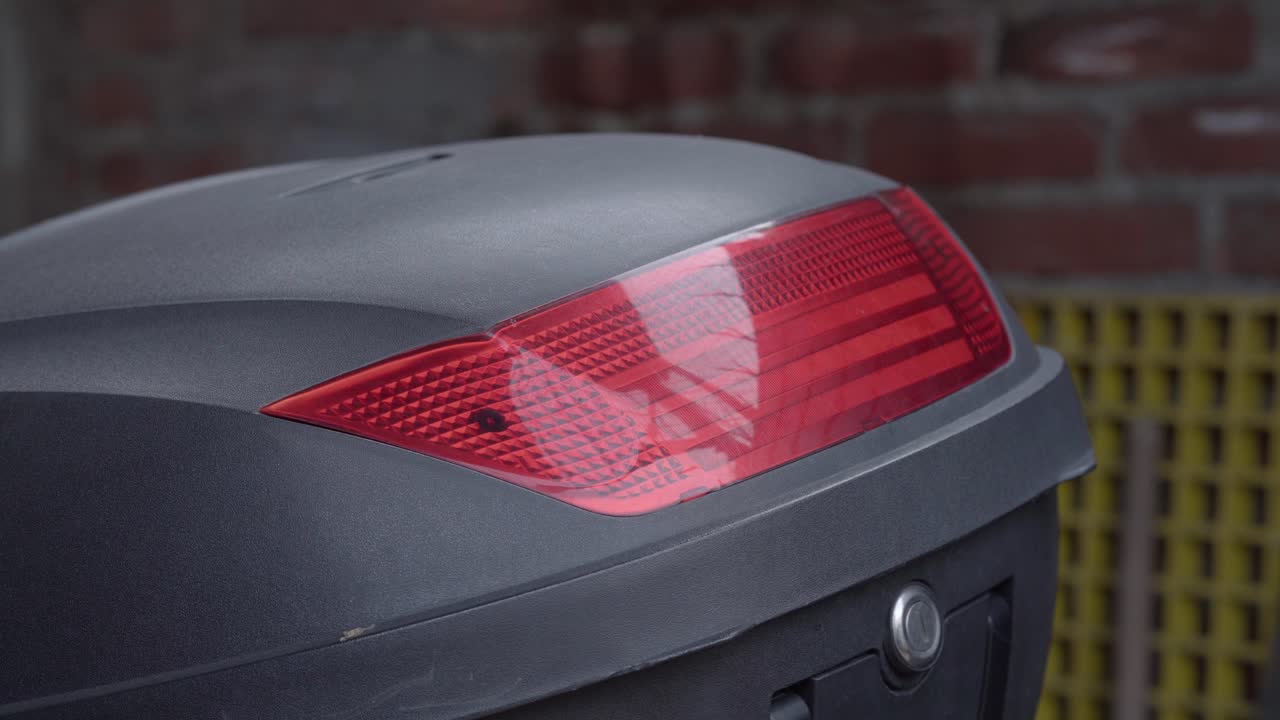 Slow panning shot showing black motorcycle trunk with red reflector inside brick wall garage