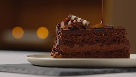 close up of melted chocolate sauce being poured onto slice of chocolate cake on plate