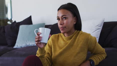 Mixed-race-woman-sitting-on-floor-drinking-a-cup-of-coffee
