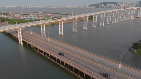 La-Inclinación-Del-Dron-Revela-Una-Toma-Del-Puente-Praia-Grande-Que-Pasa-Por-La-Carretera-Al-Lado-Del-Lago-Nam-Van,-Con-Taipa-Y-El-Puerto-Exterior-Al-Fondo