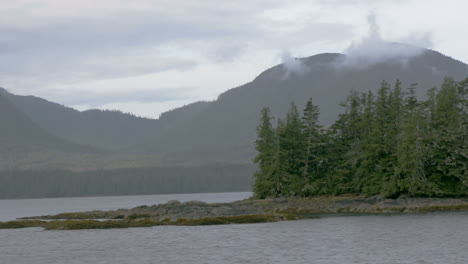 A-small-isle-of-trees-sits-in-the-center-of-an-Alaskan-fjord-as-the-camera-quickly-passes