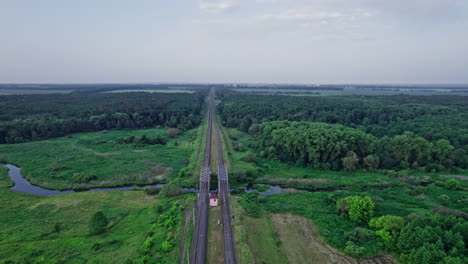 small river flows smoothly between green fields and a railway bridge