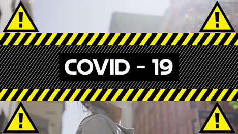 animation of text covid 19, moving over woman in face mask in sunny city street