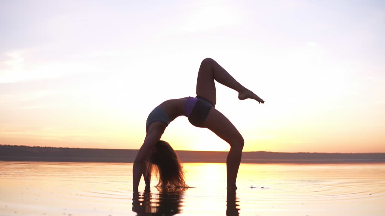 Young healthy fitness woman doing yoga, standing in bridge pose Setu Bandhasana on the seaside in the water at sunset. Enjoyment, harmony concept
