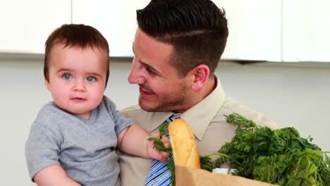 father holding his baby son and paper bag of groceries