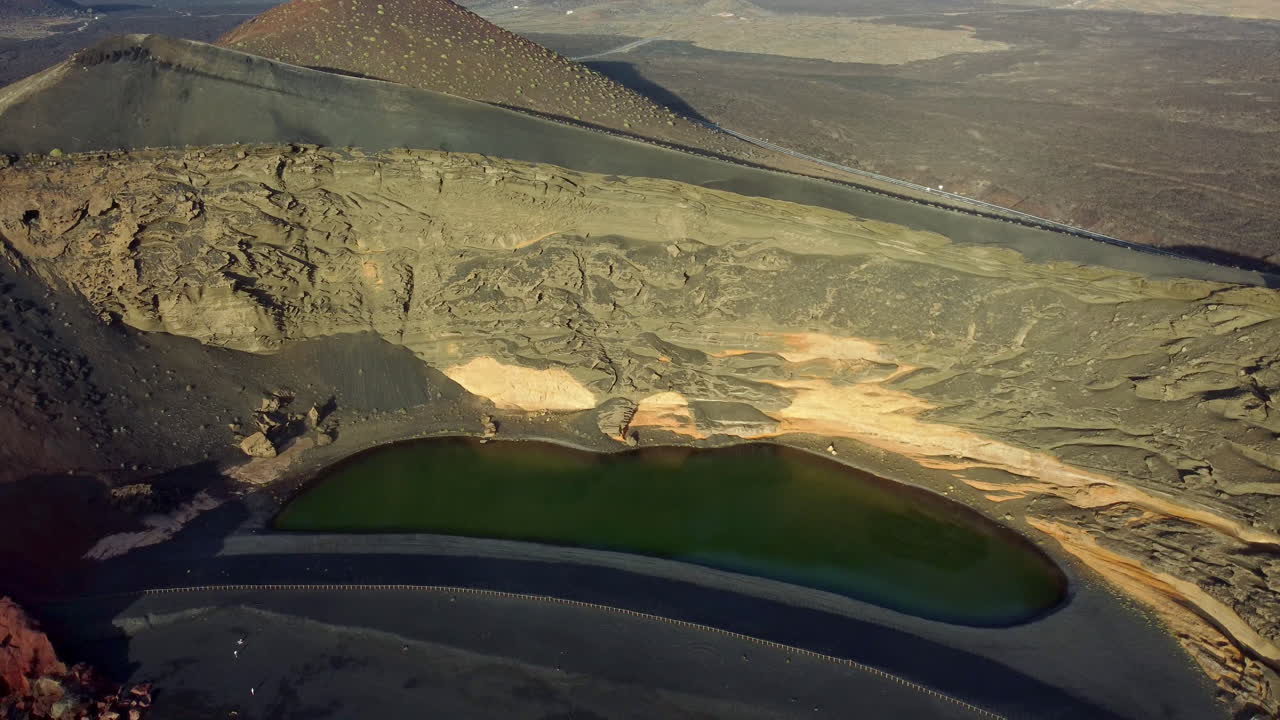 lago con agua de color verde, paisaje desértico, arena negra y montañas amarillas, la cámara desciende al agua azul con olas