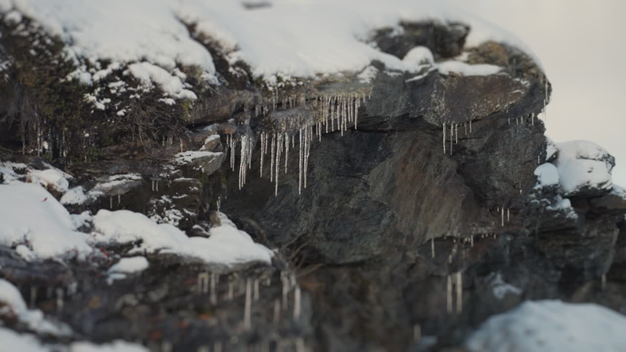 Finos e frágeis pingentes de gelo pendem das pedras cobertas de neve.