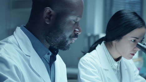 female chemist using microscope and talking to assistant during lab research
