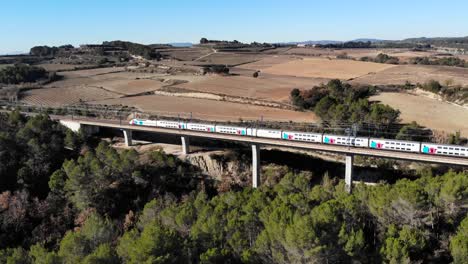 Aerial:-double-decker-high-speed-train-in-Spain-crossing-a-viaduct-between-Barcelona-and-Madrid,-in-Catalonia