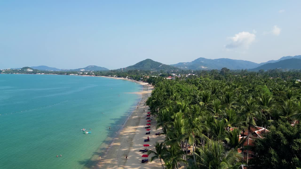 Aerial view of a beach on Koh Samui island, Thailand, featuring turquoise waters, sandy shores, and lush palm trees
