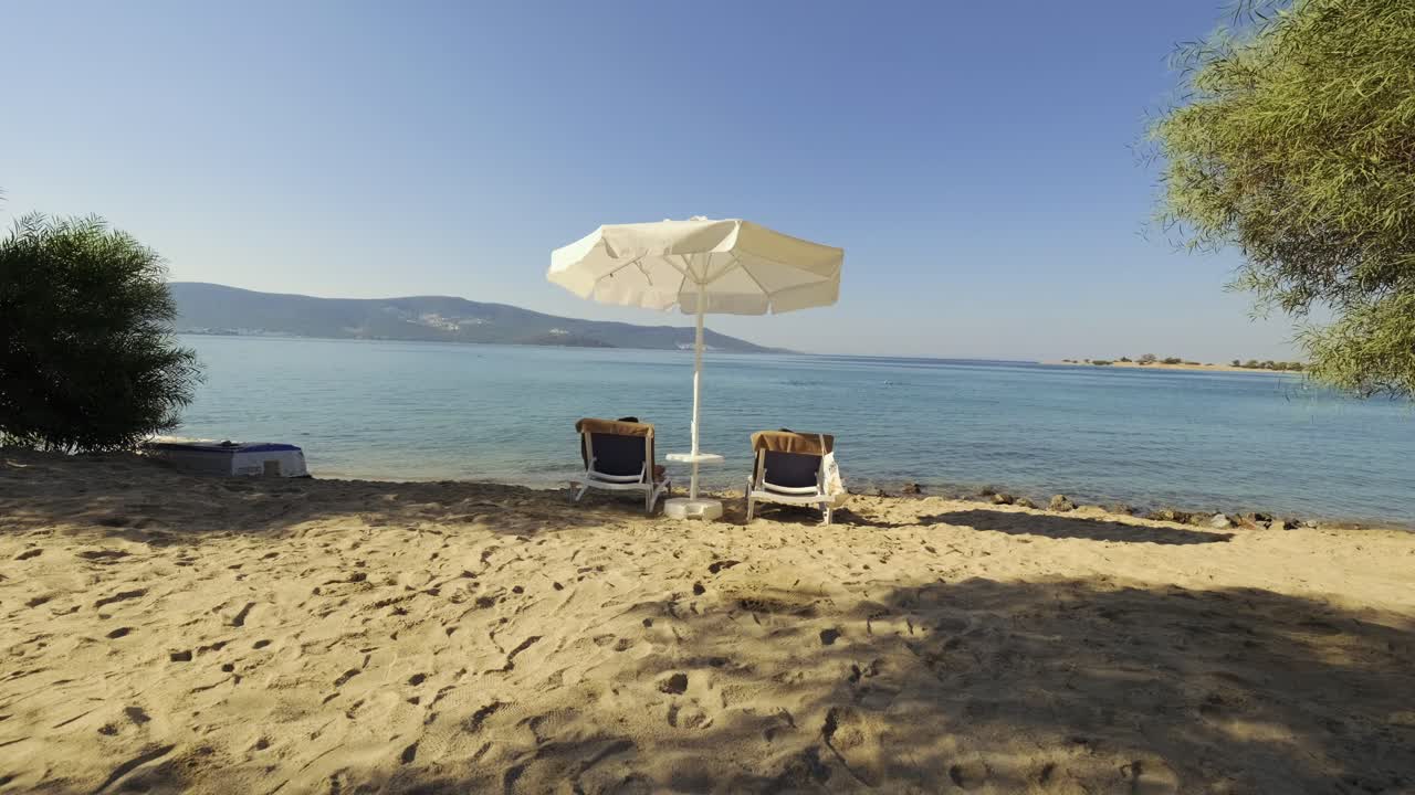 Ci sono due lettini prendisole e un ombrellone sulla spiaggia.