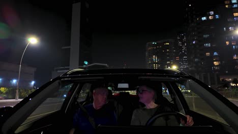 senior couple - wife driving husband through abu dhabi, united arab emirates at nighttime arguing - view from car hood looking through the windshield