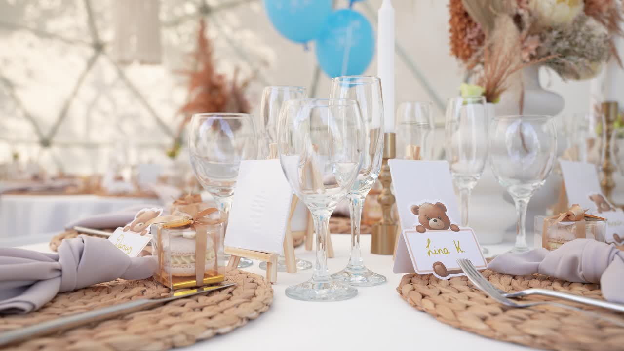 Elegant dukning för babyshower med namnbrickor med teddybjörnstema, vävda bordstabletter, vinglas och pastellfärgad dekor, vilket skapar en mysig och stilfull feststämning. Dekor för babyfödelsedag