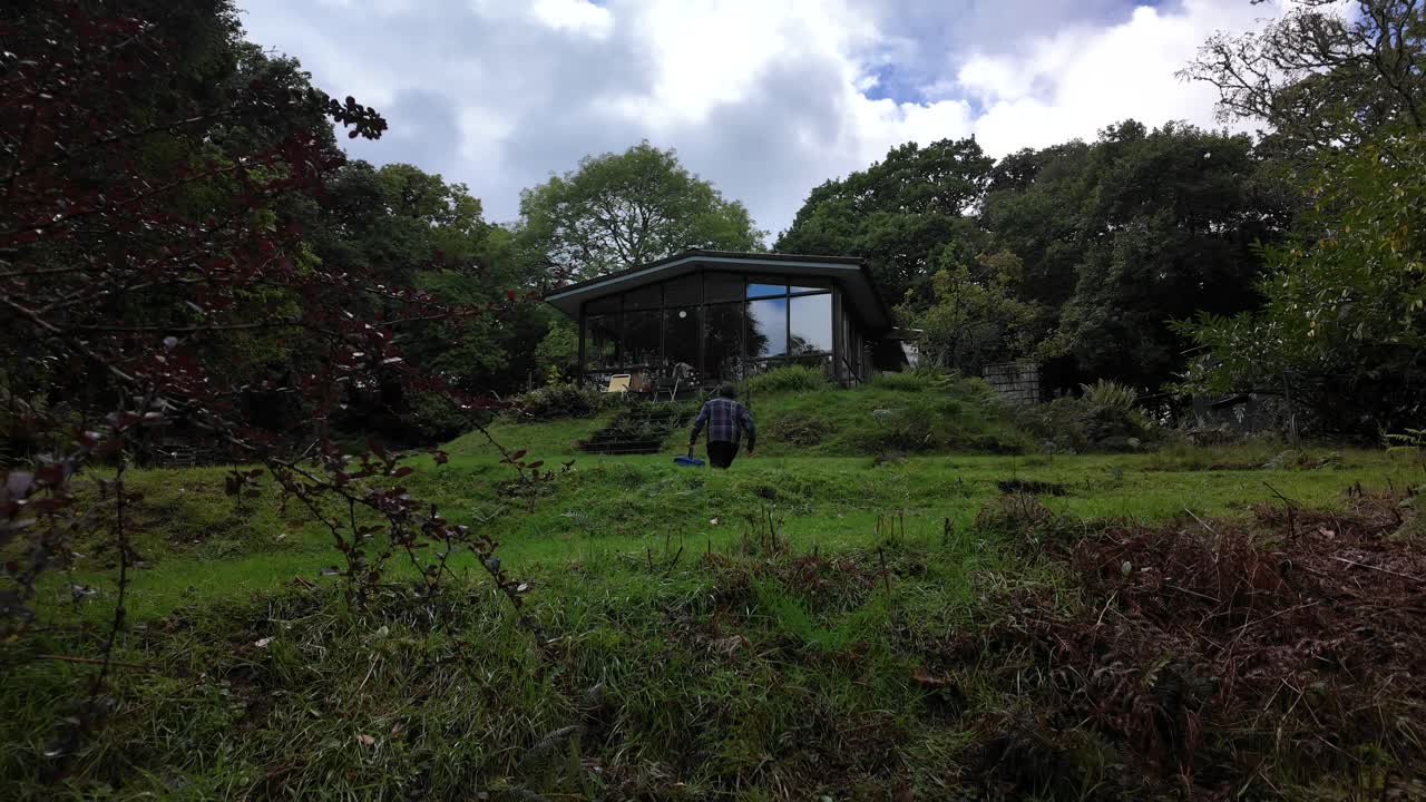 Man walking up grassy hill toward secluded cabin house in the woods
