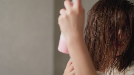 brunette lady cares for dark hair by spraying shine liquid. young woman with wet hair after washing sprays cosmetic product in toilet slow motion