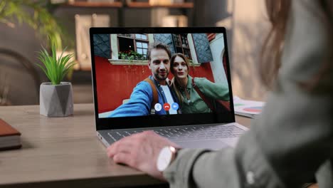 Woman-Sitting-At-Table-In-Room-And-Video-Chatting-With-Couple-Of-Happy-Friends-On-Laptop