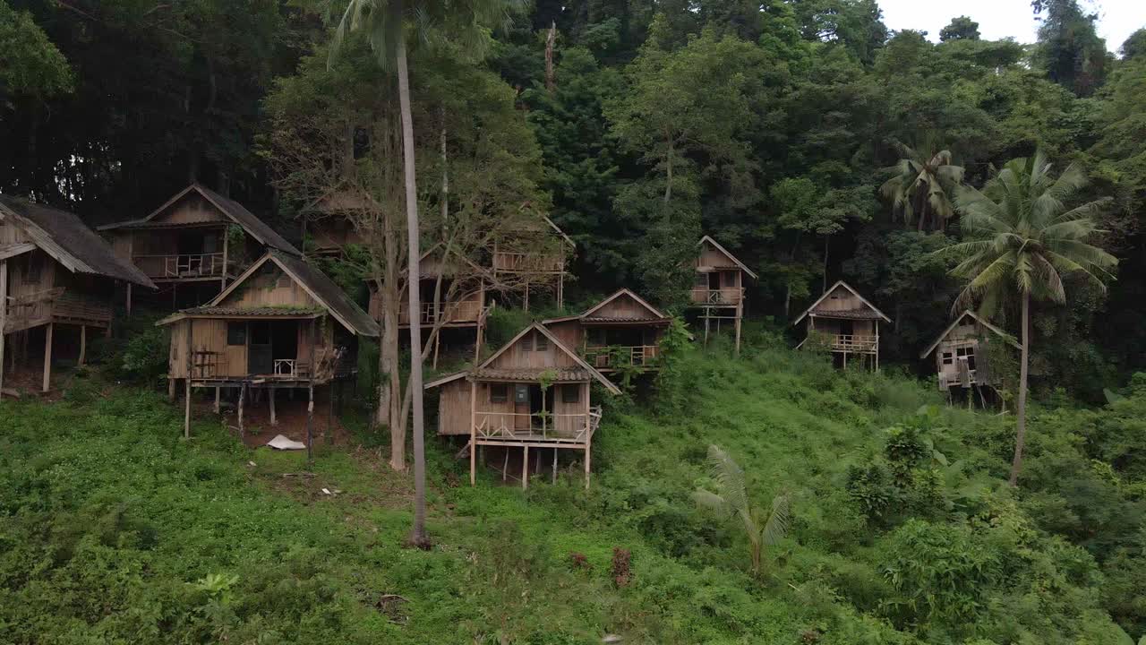 drone de tiro giratorio de camión lateral, vista aérea de pájaros de bungalows tailandeses de madera de estilo antiguo en la jungla que ahora están abandonados y sin usar debido a los efectos de la pandemia en los viajes y el turismo