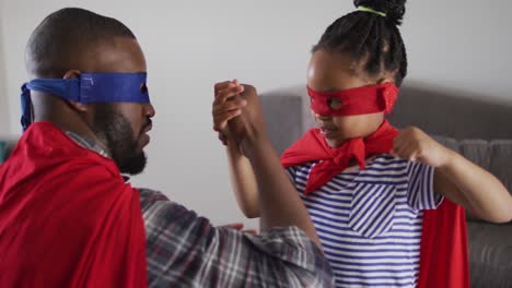 feliz hija afroamericana y padre divirtiéndose, vistiendo trajes de superhéroe