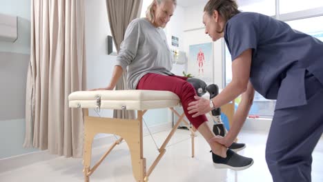 Caucasian-female-physiotherapist-stretching-leg-of-female-patient-at-rehab-center