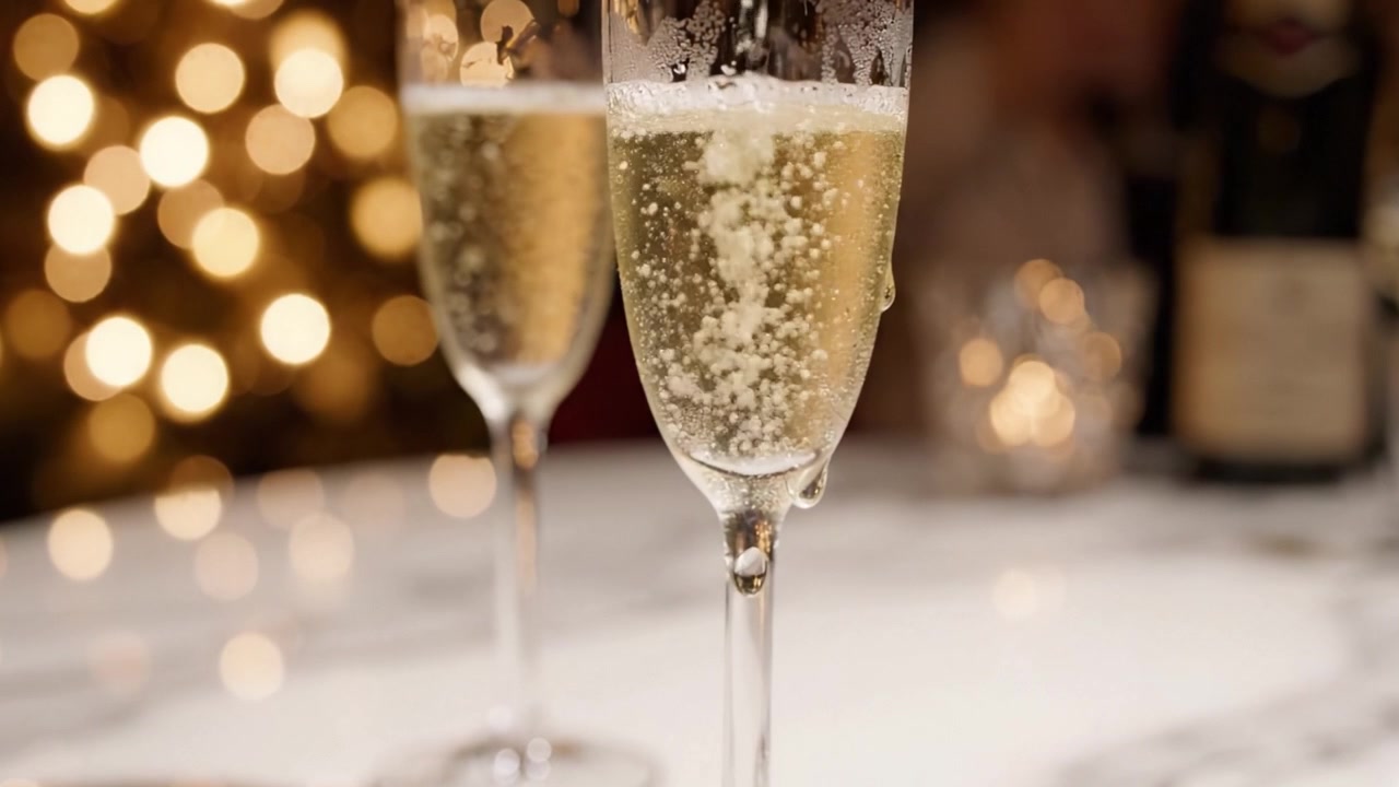 Momenti celebrativi catturati: Un paio di eleganti flûte da champagne su un tavolo di marmo che riflettono luci bokeh festive, esaltando l'atmosfera di gioia e unione.