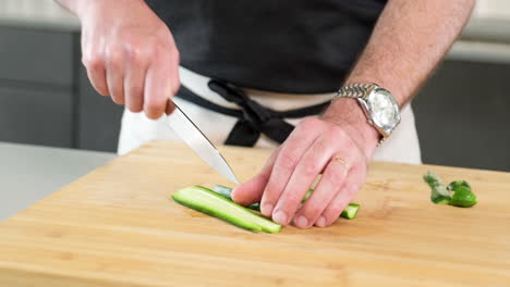 chef masculino cortando el pepino verde con la punta del cuchillo afilado