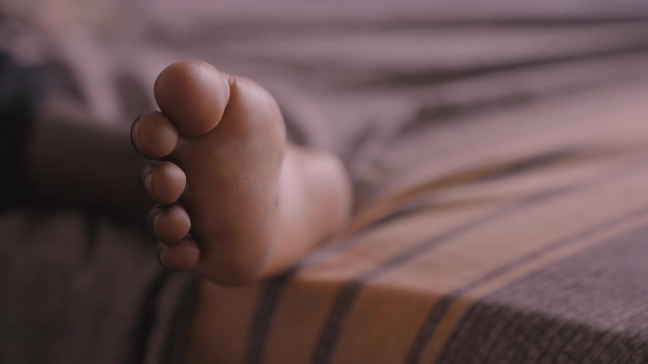 Black daughter foot resting on striped blanket, cinematic closeup, warm low light, tender newborn quiet moment, soft texture, peaceful sleep, parental care implied, cozy bedroom atmosphere