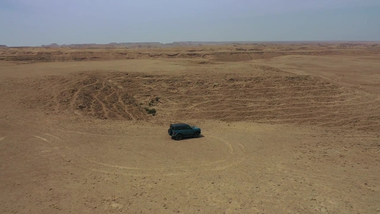 Ripresa aerea con drone di un'auto che percorre una pista sterrata isolata attraverso l'ampio e aspro altopiano desertico vicino a Edge of the World, Arabia Saudita, che mostra viaggi remoti e avventura.