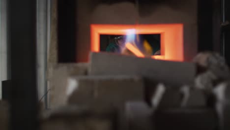 caucasian male blacksmith holding hot metal tool in kiln with tongs in workshop