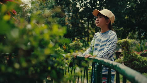 child enjoying nature, looking out over a fence in a sunny park with a serene expression