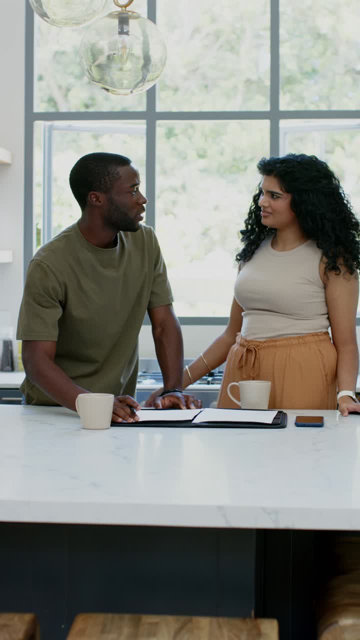 Vertical video: Diverse couple leaning on kitchen island, signing binder papers to finalize forms