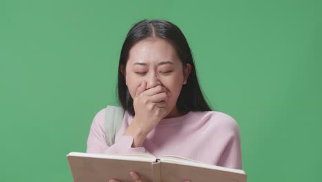 아시아 여학생이 책을 읽고 녹색 스크린 스튜디오에서 걱거리고 있습니다.