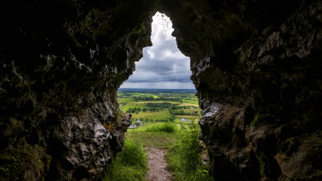 time lapse of rural farming landscape with grass fields and hills during a dark cloudy day viewed from a cave in ireland