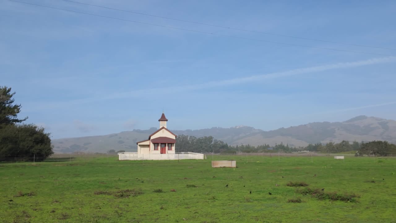 Gimbal wide panning shot of a small rural church with Hearst Castle up on the hills in the distance in San Simeon, California. 4K
