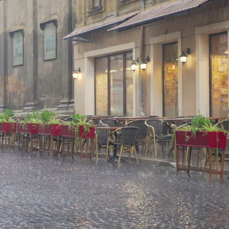 heavy raindrops falling outside on the cafe's table and chairs in the evening. big drops of rain are falling on the pavement and flower pots on the background of the empty restaurant outdoors