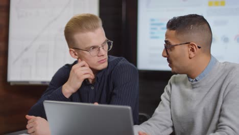 Businessman-With-Glasses-Sitting-In-Front-Of-The-Laptop,-Talks-With-Coworker-About-A-Project-In-The-Office