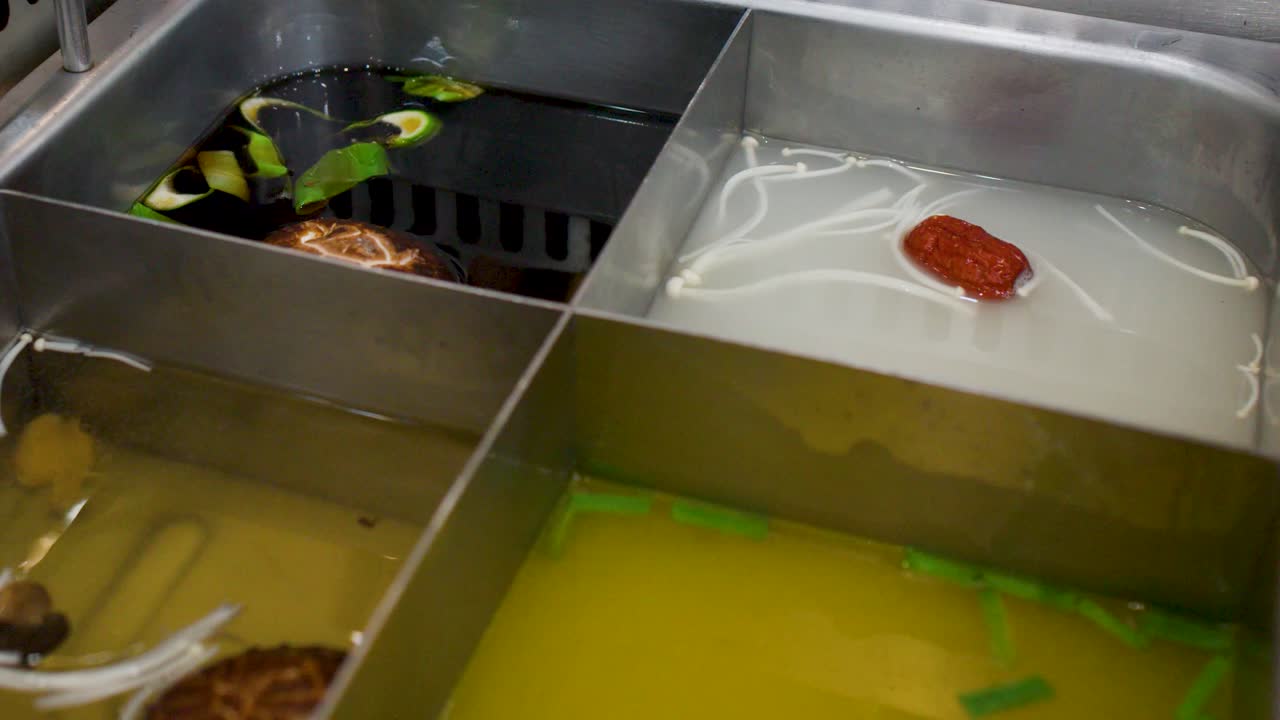 Närbild på en fyrfacks hot pot som sjuder med olika smakrika soppbaser