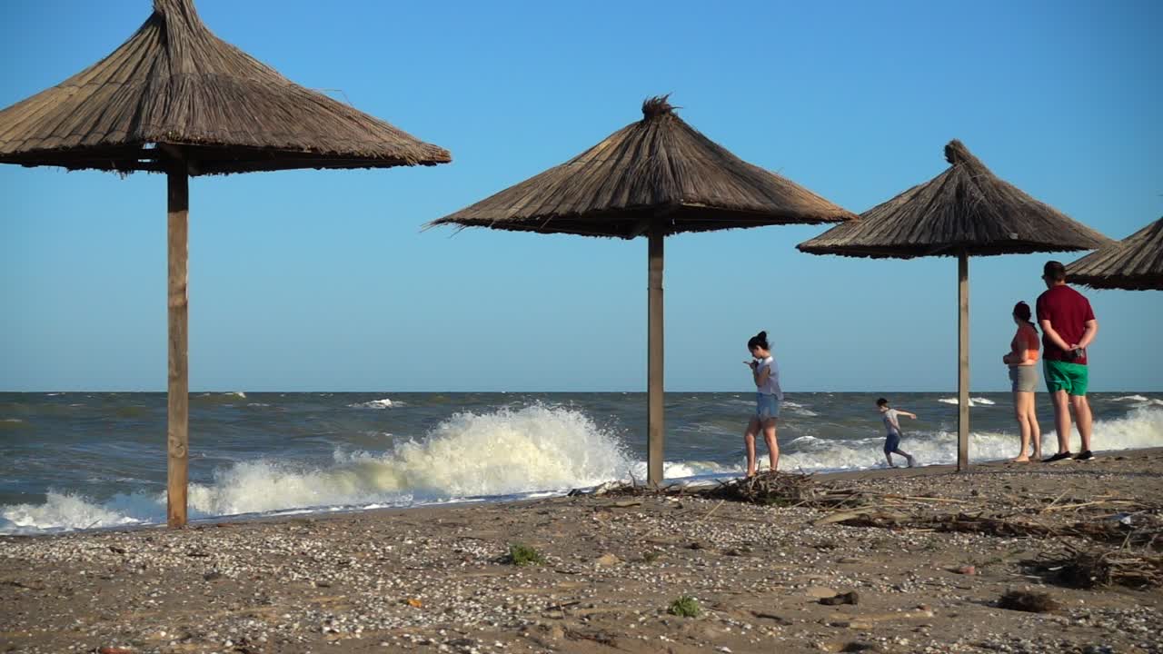 Persone che si rilassano su una spiaggia assolata con ombrelloni di paglia e onde dell'oceano