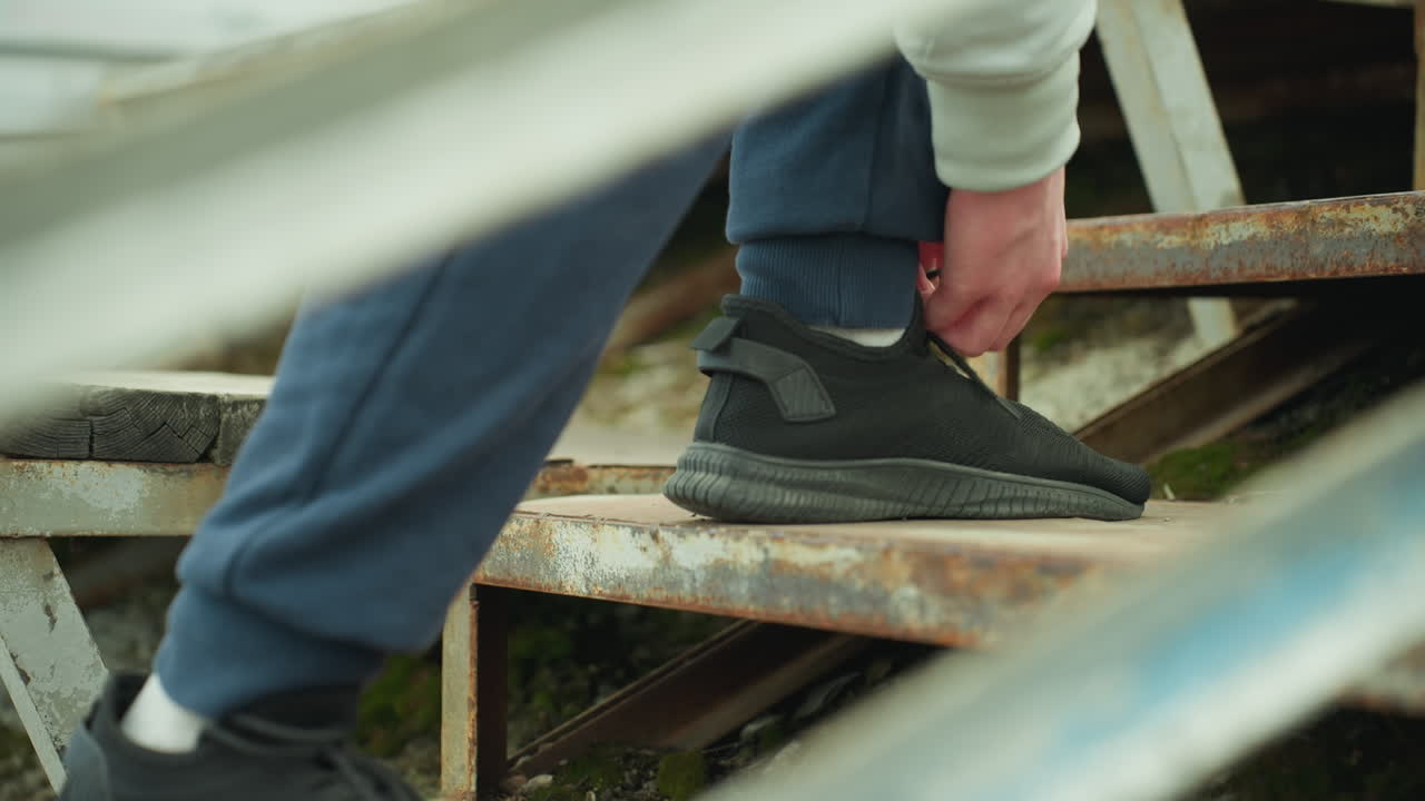 Close-up of a person bent down adjusting his shoelace while standing on a rusty staircase